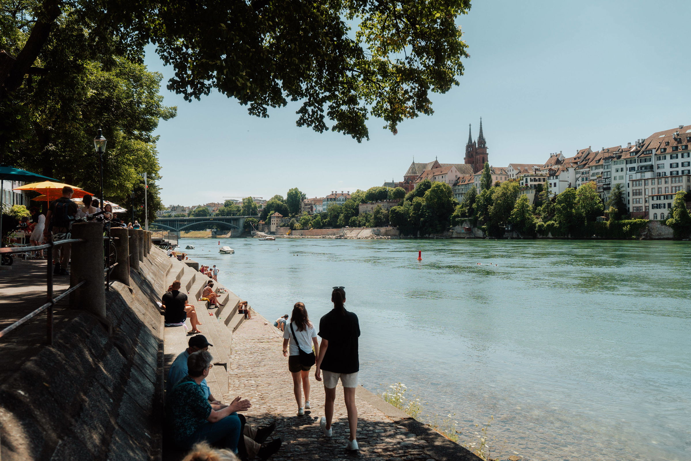 Das Rheinufer in Basel an dem junge Menschen in der Sonne spazieren