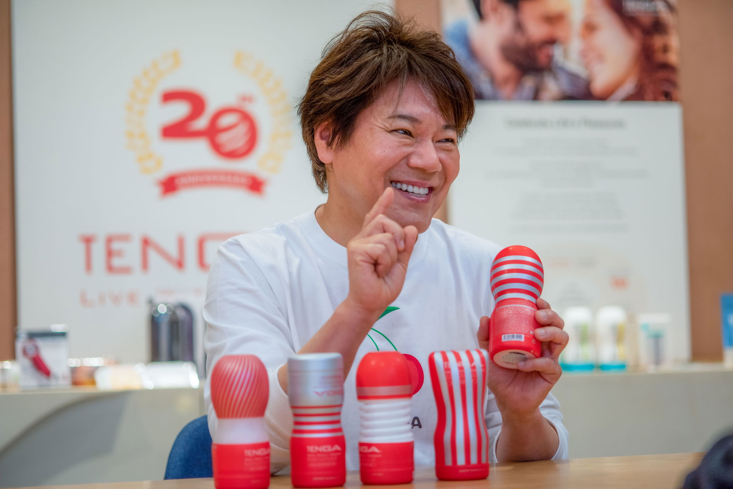 Ein Mann im weißen T-Shirt zeigt ein Produkt, das wie ein roter Zylinder aussieht. Es ist der CEO der Firma Tenga mit seinen Sex-Toys